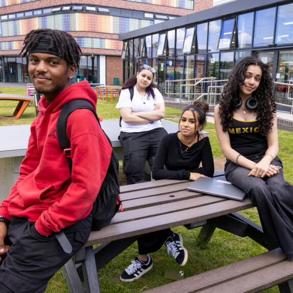 Student standing and sitting around a picnic table outside the Loughborough College 1909 Lounge student space